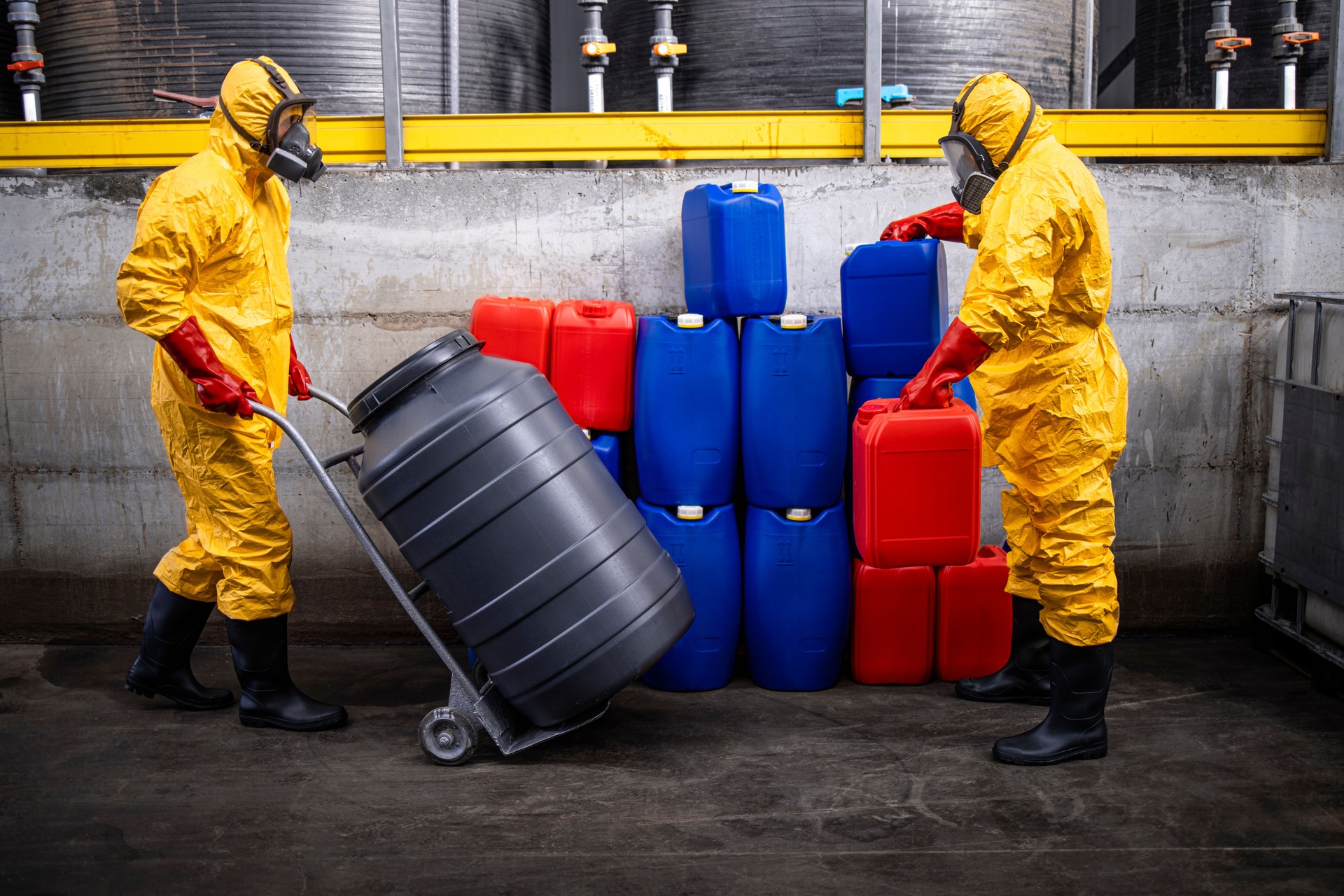 Chemical plant workers  in protection suit handling barrels and canisters with chemicals inside production factory.